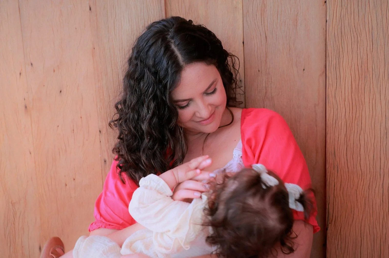 Majka nježno doji svoju bebu pored drvenog zida.