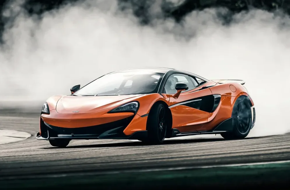 Narandžasti McLaren automobil u driftu sa puno dima oko zadnjeg točka