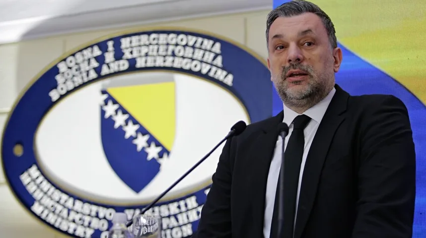 Političar u crnom odijelu s crnom kravatom govori za govornicom.