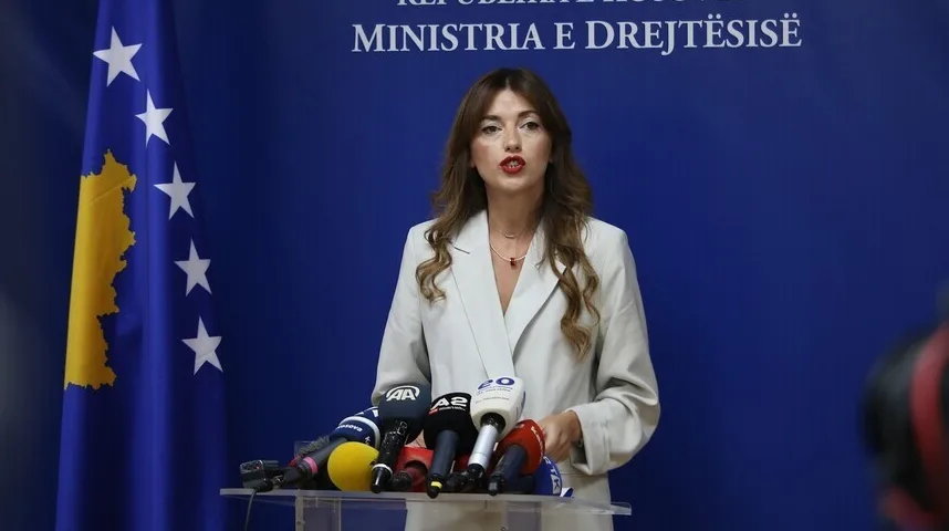 Ministarka pravde Kosova drži govor pred medijima pored zastave Kosova.