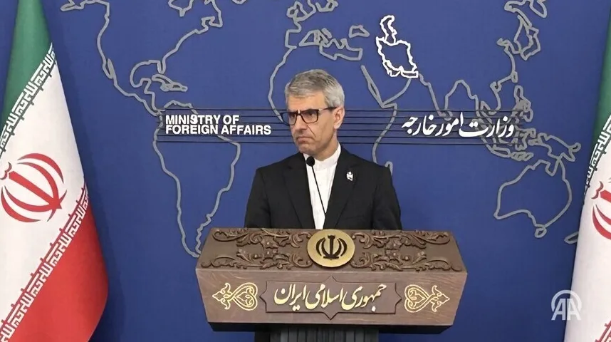 Muškarac u crnom odijelu i bijeloj košulji, sa naočarima, stoji iza govornice sa amblemom Irana, ispred plave pozadine sa iscrtanom kartom svijeta i zastavama Irana.