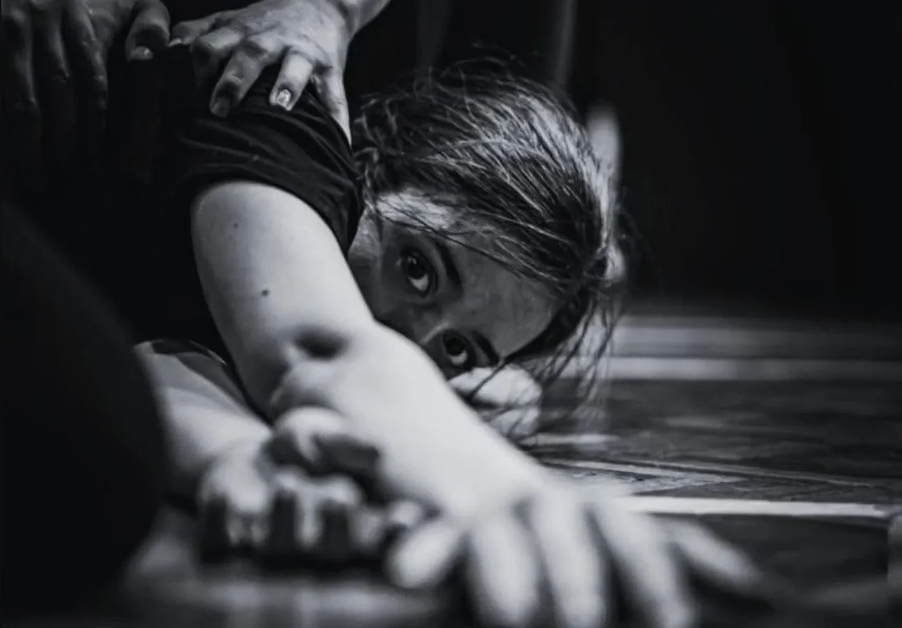 Intenzivan pogled mlade plesačice koja leži na podu, s rukama ispruženim ispred sebe.