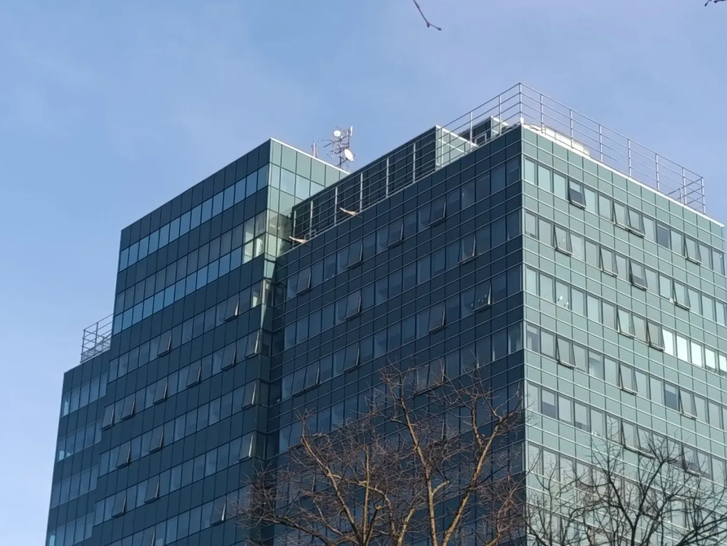 Modernu poslovnu zgradu sa staklenom fasadom i antenskim sistemom na vrhu.