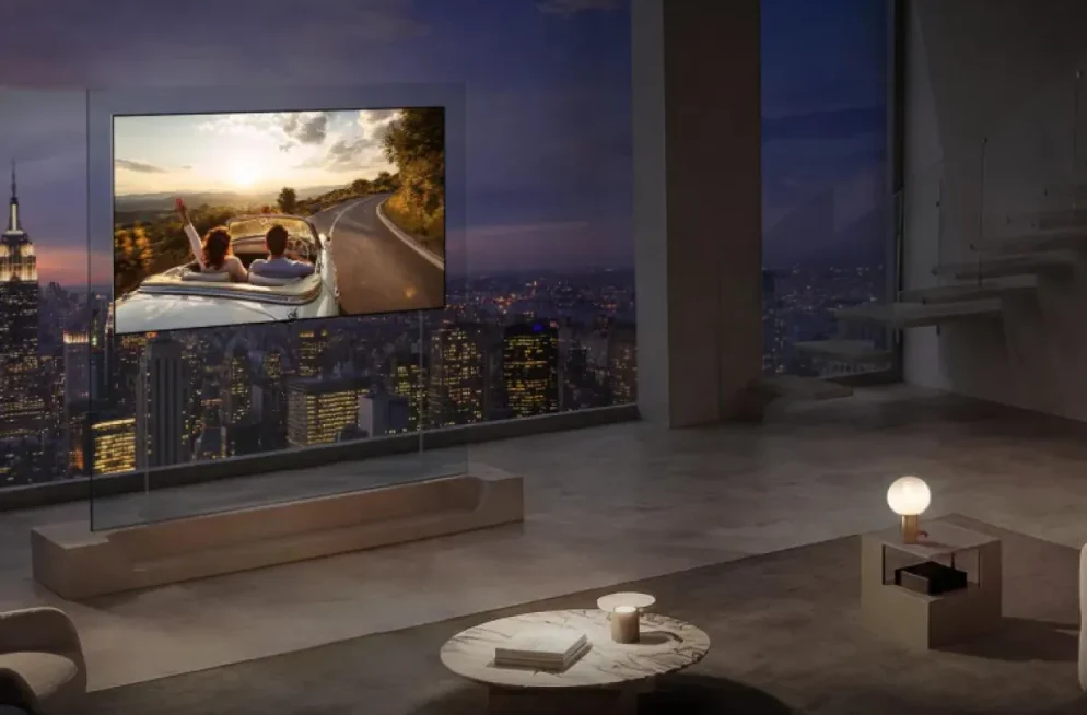 Luksuzni dnevni boravak sa modernim, gotovo prozirnim televizorom koji prikazuje par u kabrioletu na zalasku sunca, uz panoramski pogled na gradsku panoramu noću.