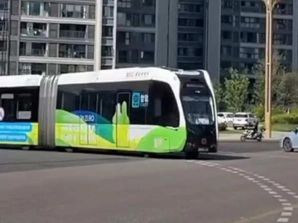 Moderni tramvaj sa zelenim i bijelim dizajnom koji prolazi kroz gradski kružni tok.