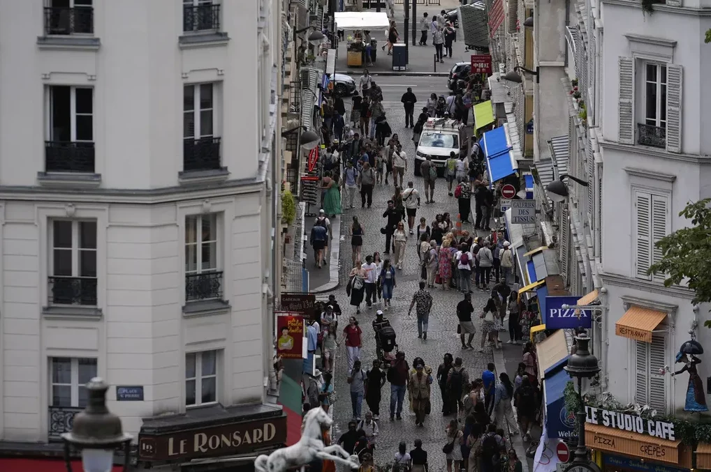 Gornji pogled na prepunu ulicu na Montmartreu u Parizu, s ljudima koji šetaju između zgrada i trgovina.
