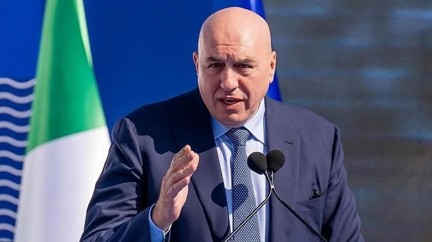 Ćelav muškarac u tamnoplavom odijelu sa plavom košuljom i bijelom kravatom s plavim tačkicama, drži govor ispred mikrofona.