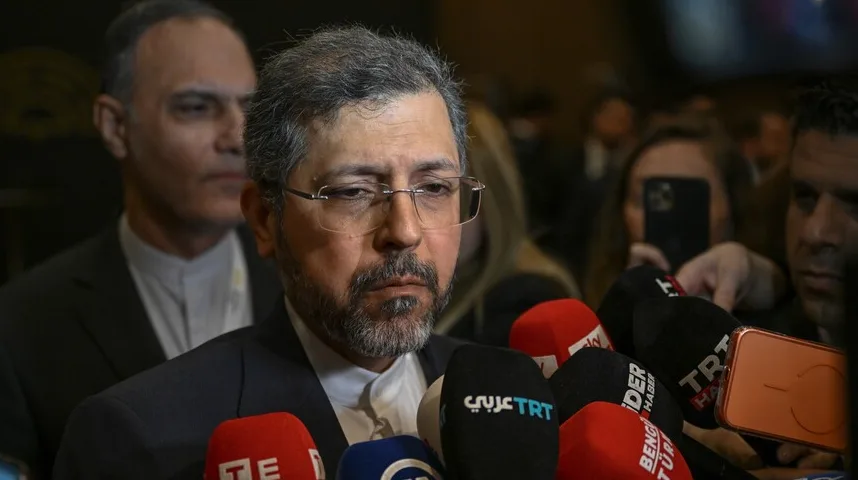 Portret muškarca sa naočalama i bradom, okruženog mikrofonima medija, dok se iza njega nazire druga osoba.