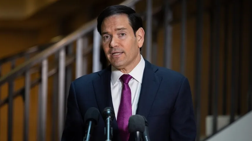 Muškarac u tamnom odijelu i ljubičastoj kravati govori za govornicom ispred mikrofona.