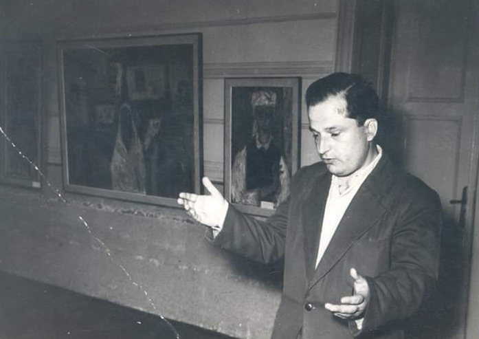 Muškarac gestikulira rukama dok objašnjava izložene slike u galeriji.