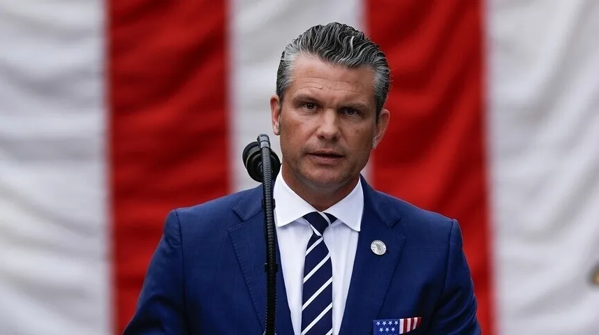 Političar u tamnom odijelu, bijeloj košulji i plavo-bijeloj prugastoj kravati govori iza mikrofona. Na desnoj strani revera mu je značka, a na džepu patriotski džepni rubac sa zvijezdama i prugama Sjedinjenih Američkih Država. U pozadini se nazire zastava SAD-a sa crvenim i bijelim prugama.