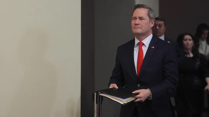 Muskarac u tamnom odijelu i crvenoj kravati, noseći fasciklu sa dokumentima.