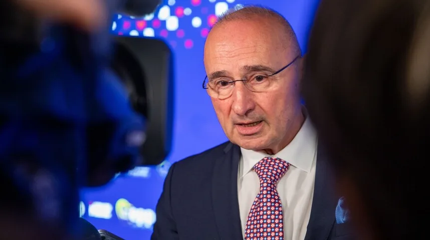 Muškarac u tamnoplavom odijelu, bijeloj košulji i šarenim dezeniranim sakoom, sa naočarima na očima.