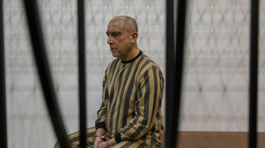 Muškarac u zatvoru, obučen u prugastu odjeću, sjedi iza rešetaka.