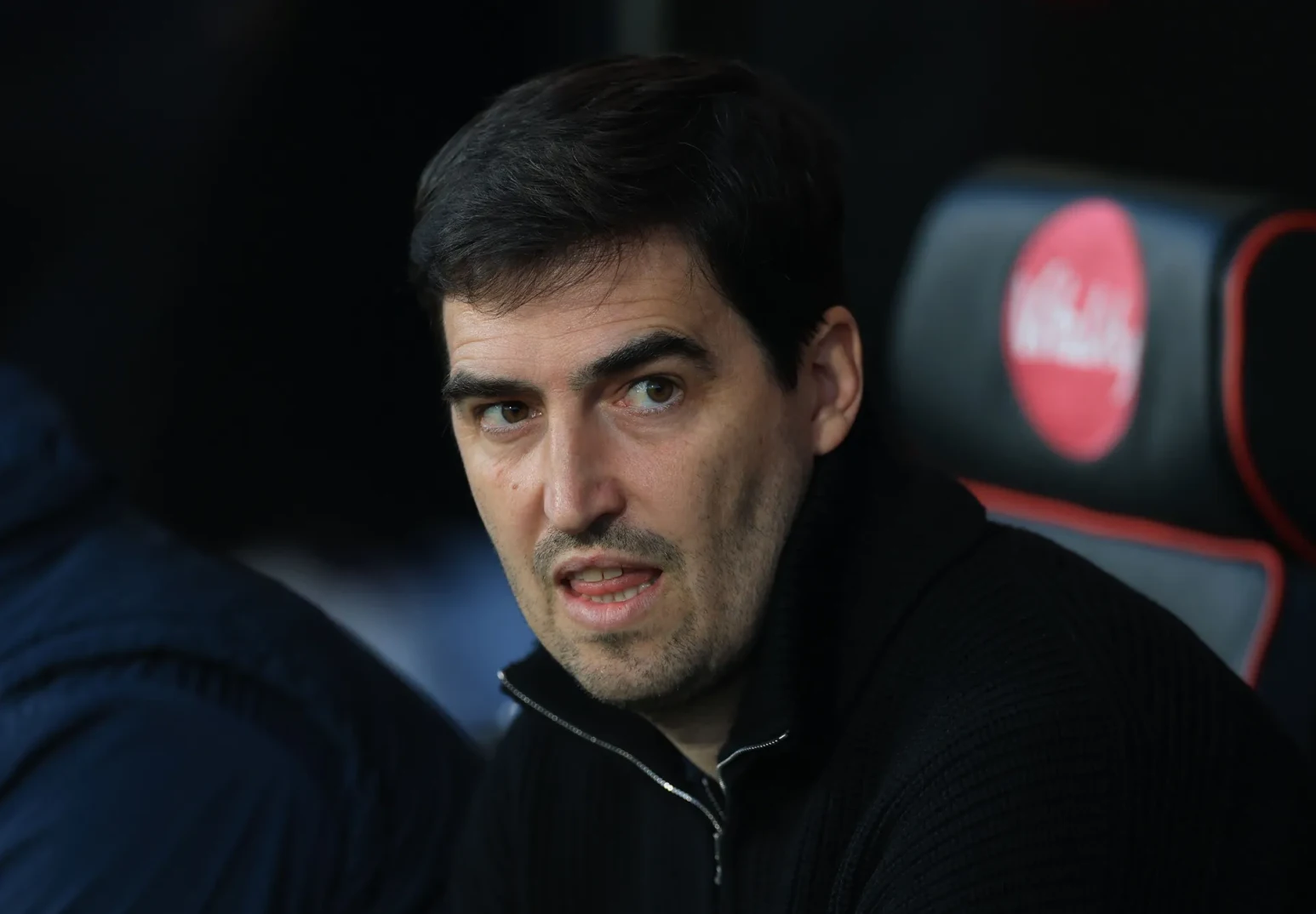 Krupni kadar muškog lica sa tamnom kosom i bradom, obučen u crni džemper sa cibzarom.