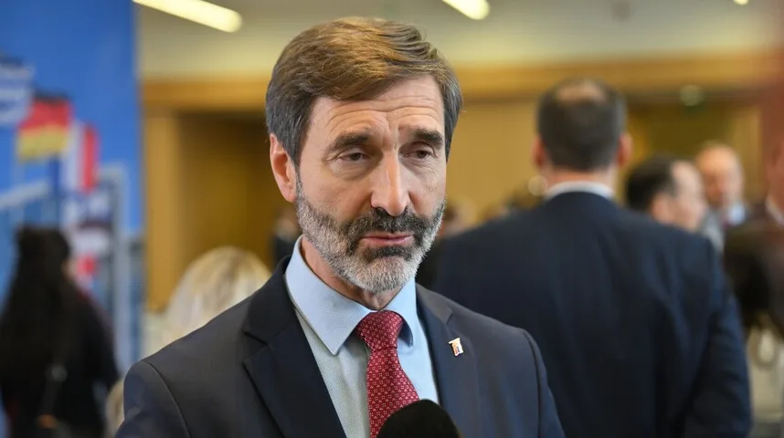 Čovjek sa bradicom i crvenom kravatom gleda prema mikrofonu.