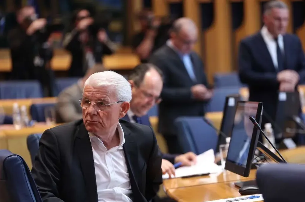 Političar sa bijelom kosom i naočalama sjedi u skupštinskoj sali