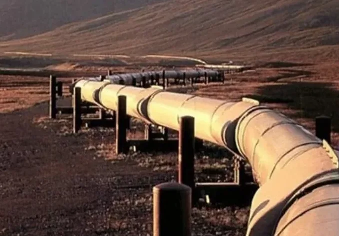 Žuti naftovod koji se proteže kroz suvo, pustinjsko područje sa brdima u pozadini.