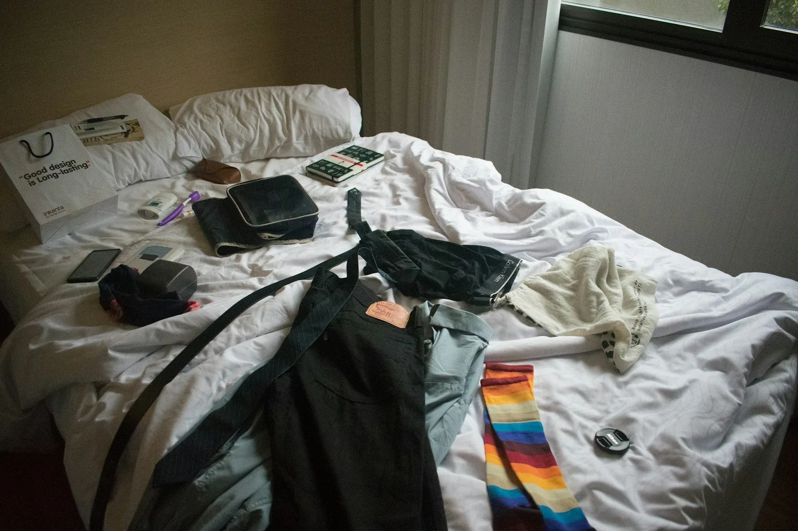 Nepospremljen krevet sa odjećom, obući, toaletnim potrepštinama i jednom torbicom.