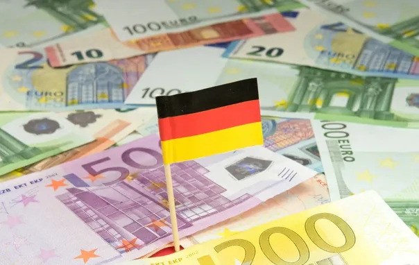 Njemačka zastavica zabodena u hrpu novčanica eura različitih apoena.