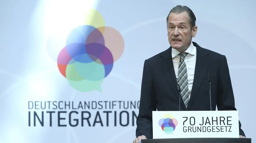 Političar u crnom odijelu govori iza govornice na događaju.