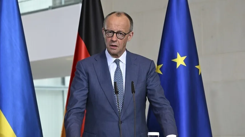 Njemački političar u plavom odijelu i bijeloj košulji s plavo-bijelom kravatom govori iza govornice, s njemačkom i zastavom Evropske unije iza njega.