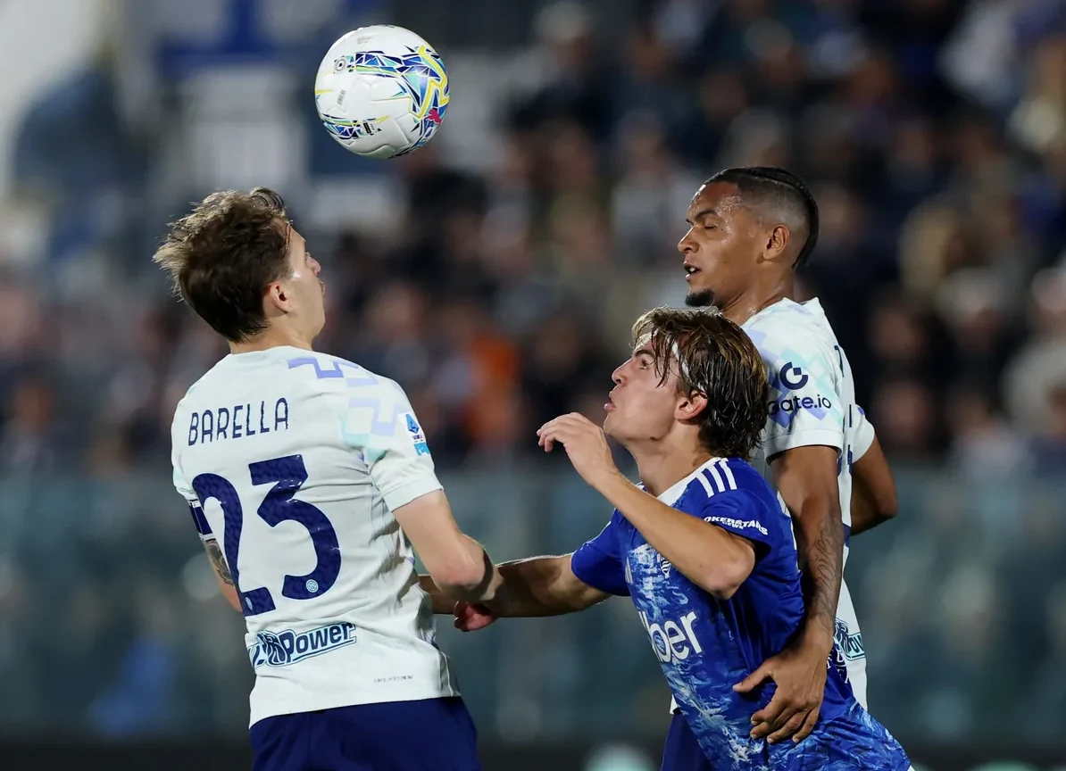 Fudbaleri se bore za loptu u zraku na stadionu, fokusirani na nadolazeći udarac glavom.