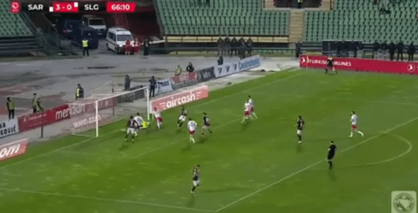 Fudbaleri u bijelim i crnim dresovima na fudbalskom terenu tokom utakmice.