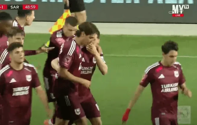 Fudbaleri u bordo dresovima slave gol na terenu.