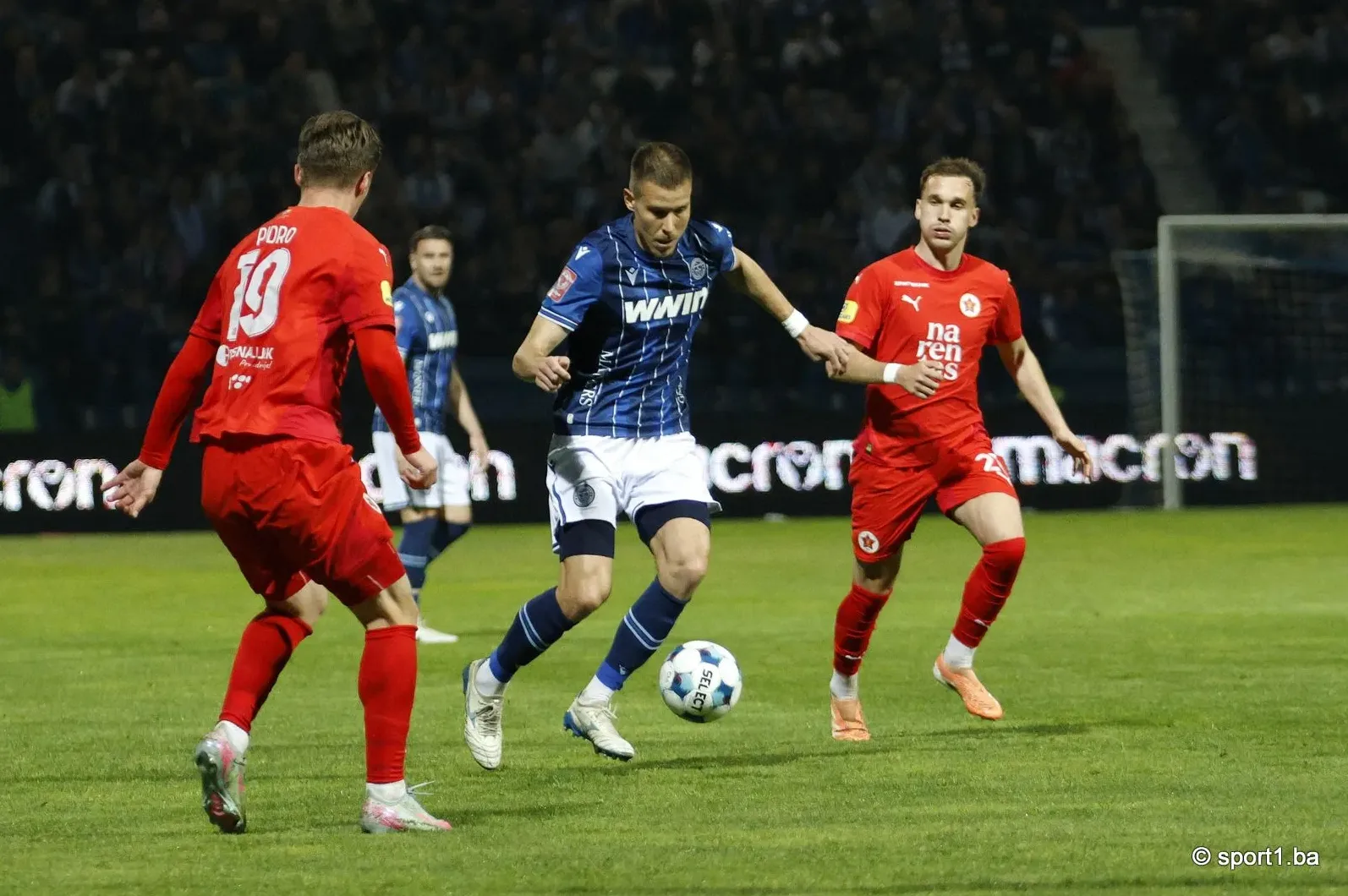 Fudbaleri u crvenim i plavo-bijelim dresovima bore se za loptu na terenu