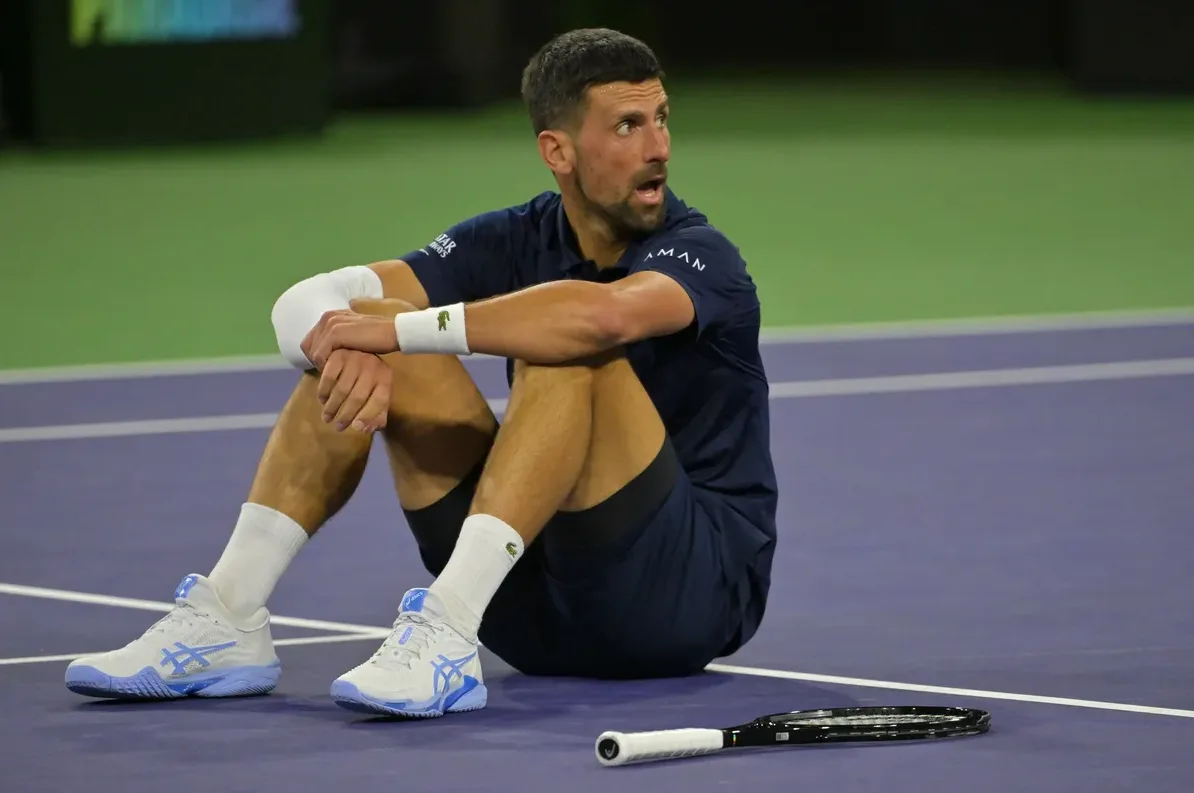 Novak Đoković sjedi na teniskom terenu, naslonjen na koljena.