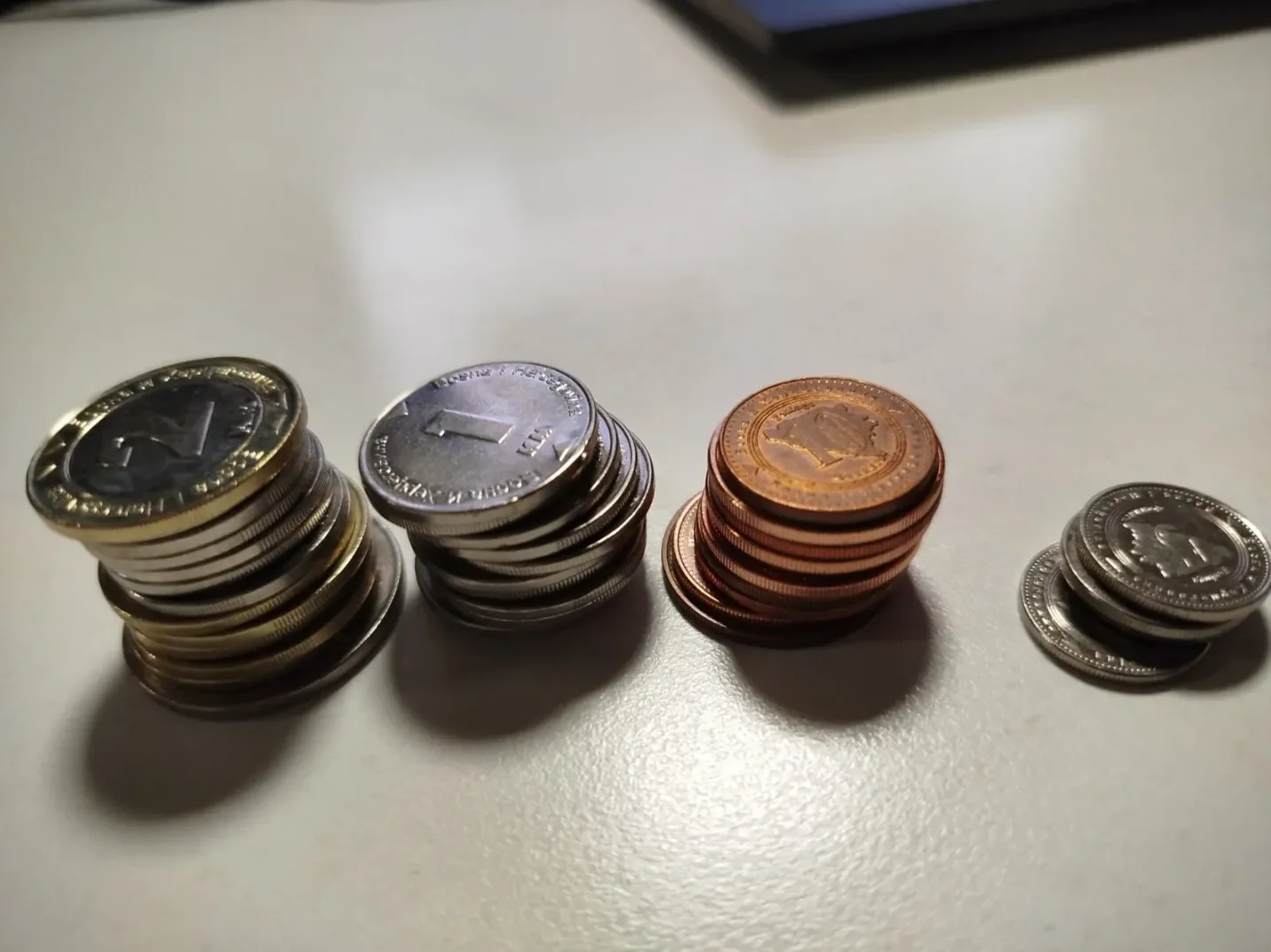 Snimak gomila metalnih novčića različitih veličina i boja, postavljenih na bijelu površinu.