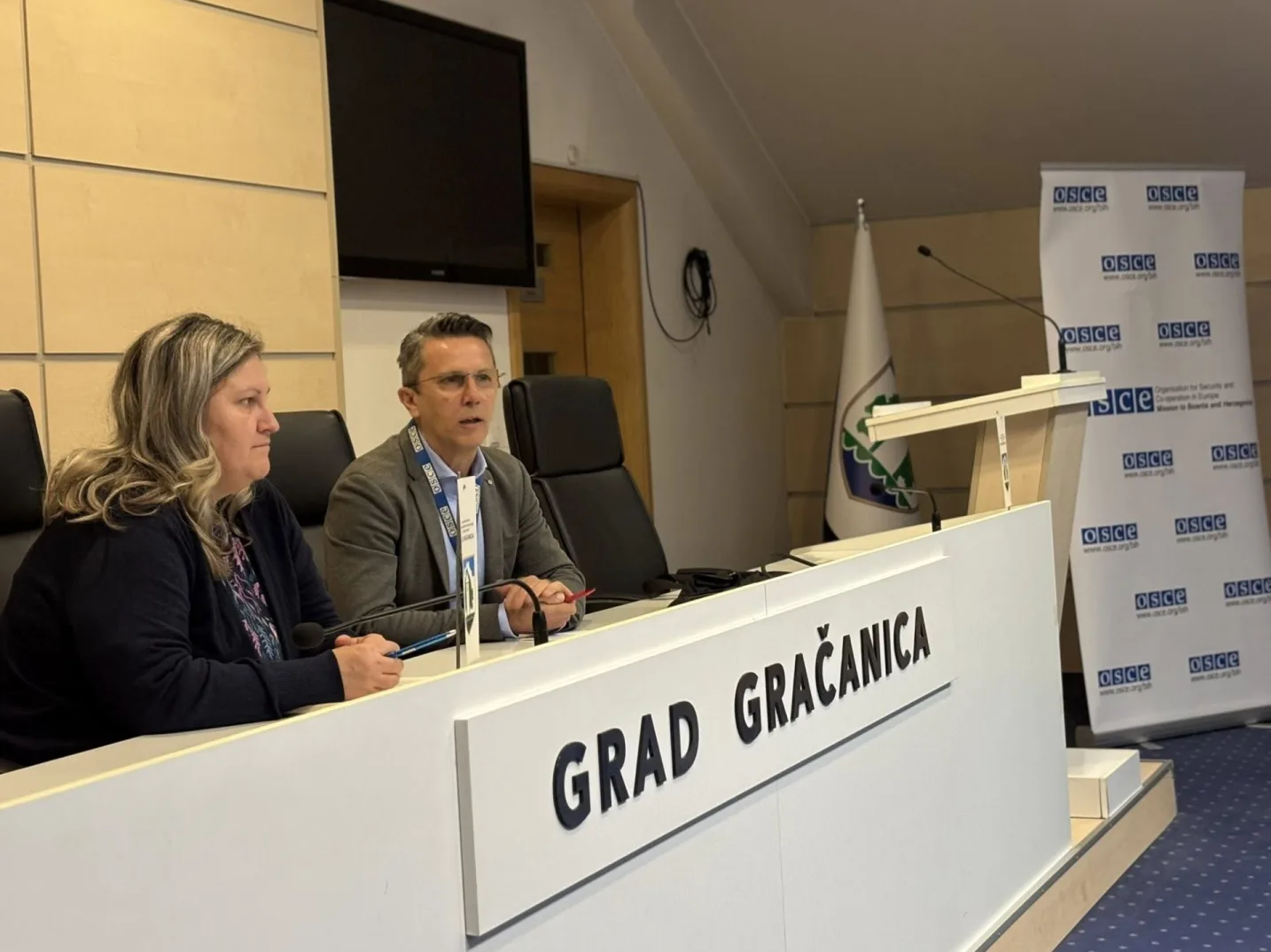 Muškarac i žena sjede za stolom na konferenciji ispred natpisa "GRAD GRAČANICA".