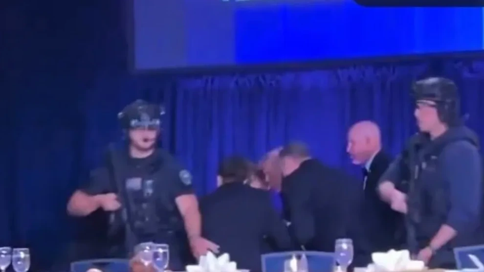 Snimak prikazuje osoblje obezbjeđenja u taktičkoj opremi, uključujući kacige i pancire, kako intervenišu ili stoje u pripravnosti na događaju iza plave zavjese.