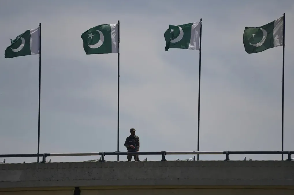 Četiri zastave Pakistana vijore se na vjetru, a ispod njih stoji vojnik u uniformi na zidu.