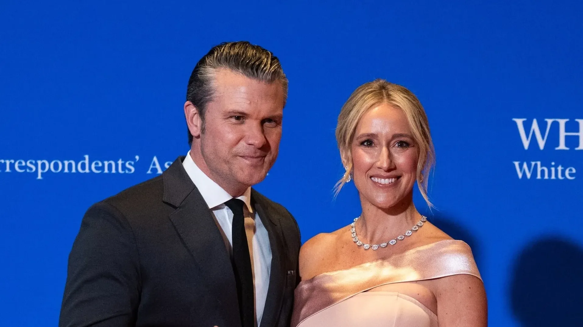 Muškarac u tamnom odijelu i žena u bež haljini sa dijamantskom ogrlicom nasmijani na događaju Bijele kuće