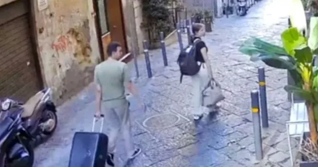 Mladić i djevojka sa prtljagom hodaju uskom ulicom popločanom kaldrmom.