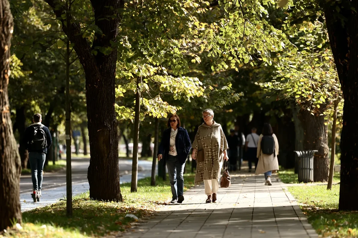 Dvije žene šetaju stazom u parku pod jesenjim drvećem.