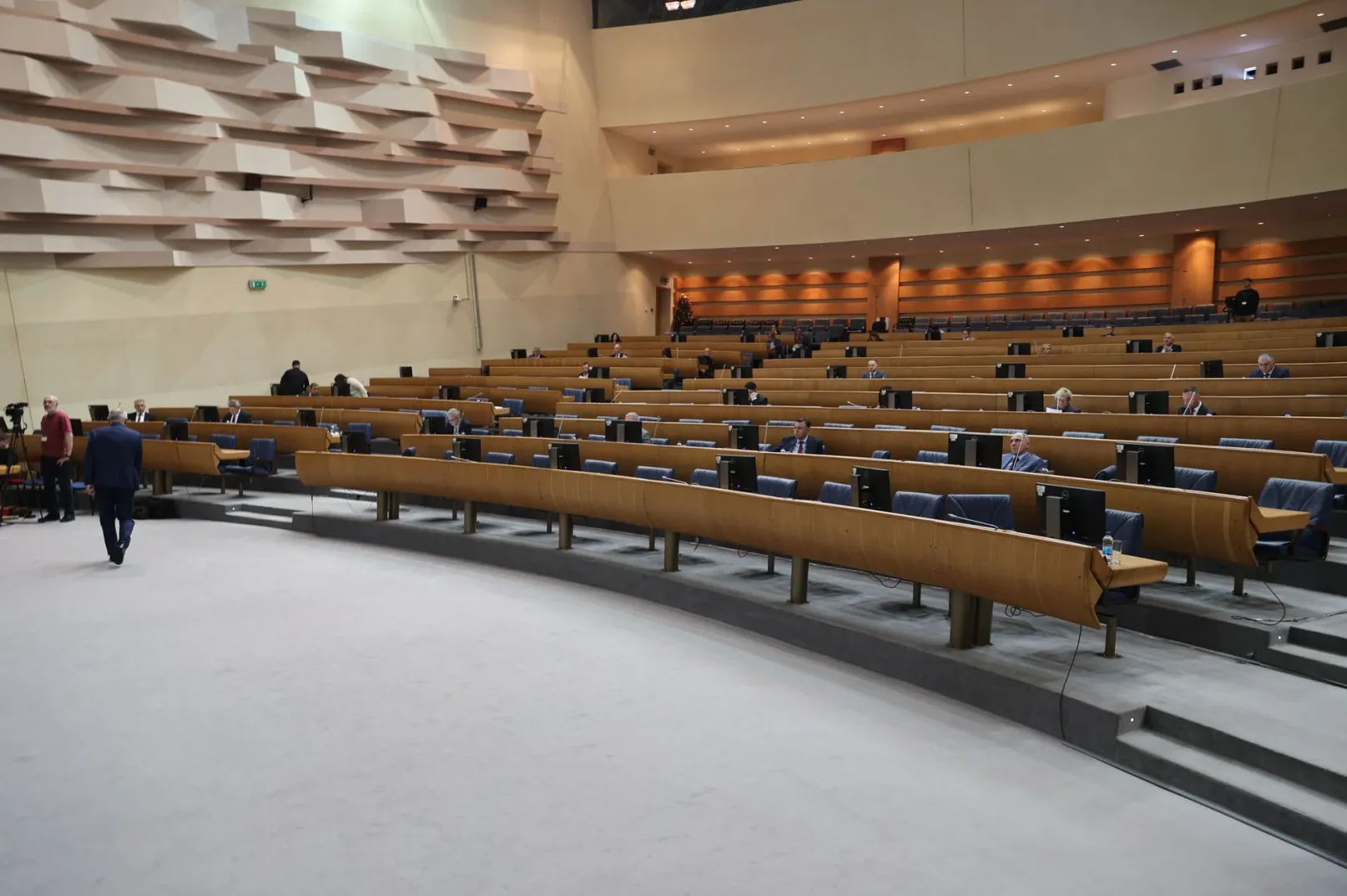 Sala za sjednice sa redovima stolica i stolova, gdje sjede ljudi u odijelima