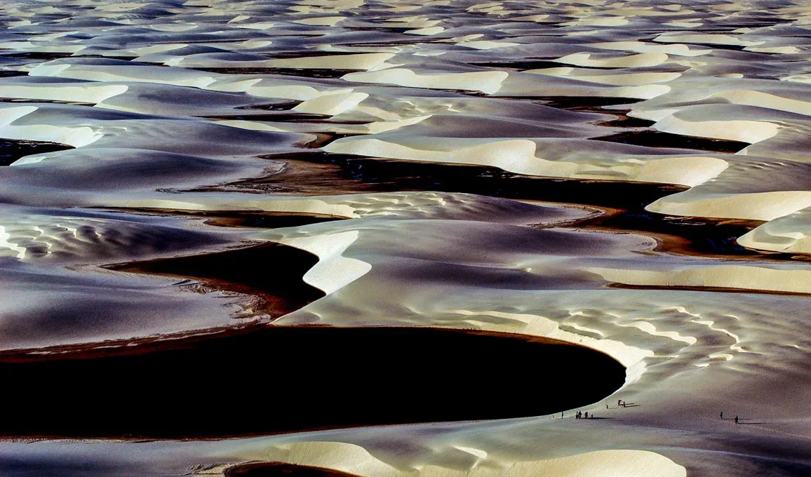 Zračni pogled na beskrajne pješčane dine isprepletene tamnim vodenim površinama, koje stvaraju zadivljujući kontrast.