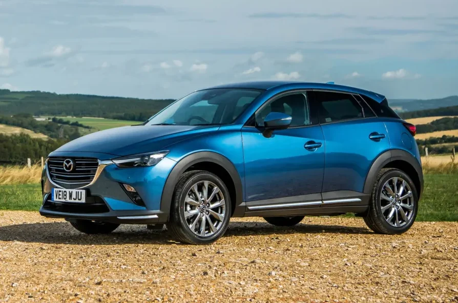 Plavi Mazda CX-3 automobil parkiran na makadamskom putu ispred zelenih brežuljaka.