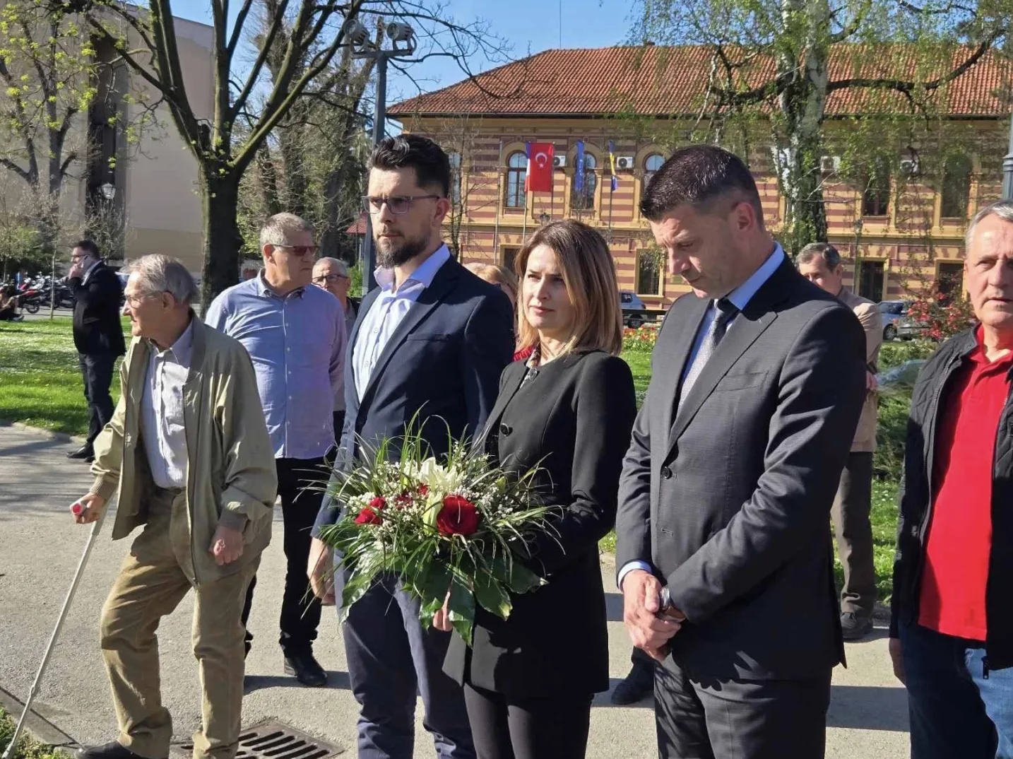 Grupa zvaničnika i građana polaže vijenac ispred zgrade sa zastavama na jarbolima
