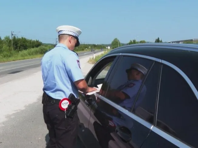 Policajac u uniformi zaustavlja crni automobil i pregleda dokumenta vozaču.