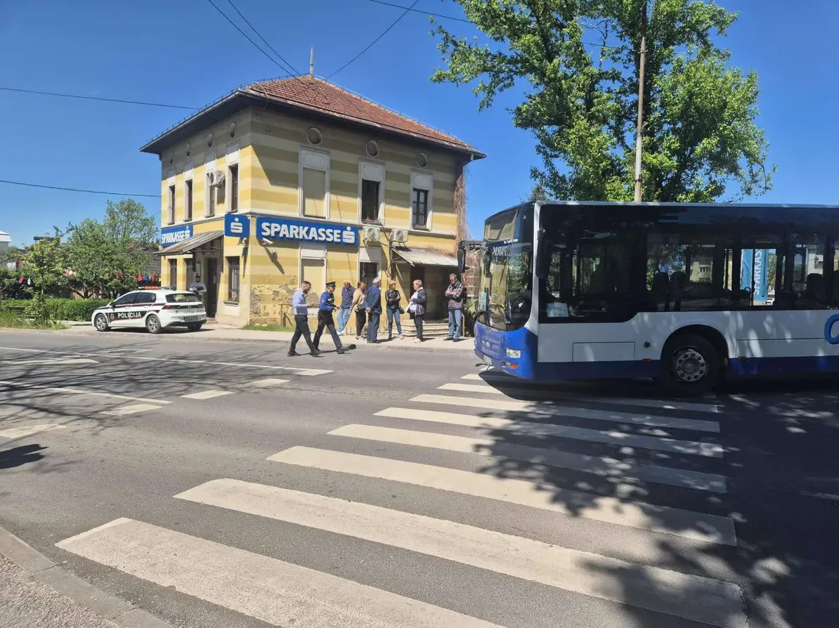 Autobus javnog prevoza na pješačkom prelazu ispred zgrade Sparkasse banke, pored policijskog vozila.