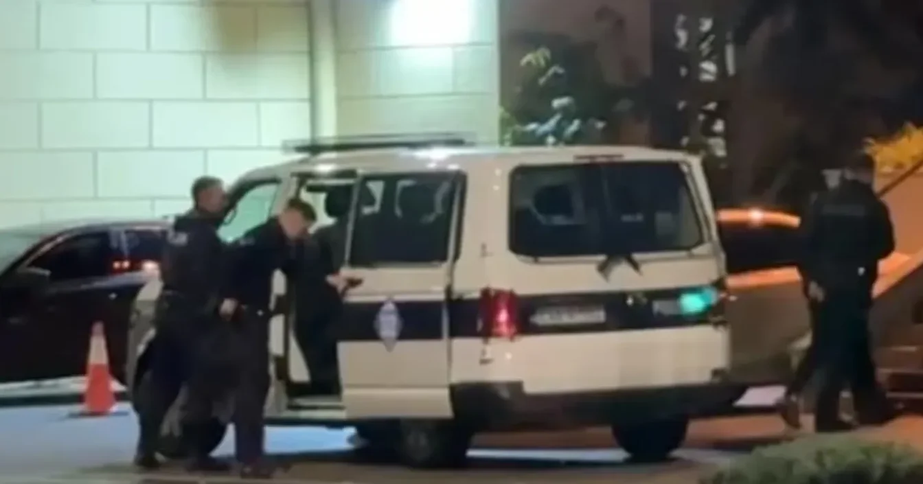 Policijski službenici dovode uhapšenu osobu do policijskog kombija.