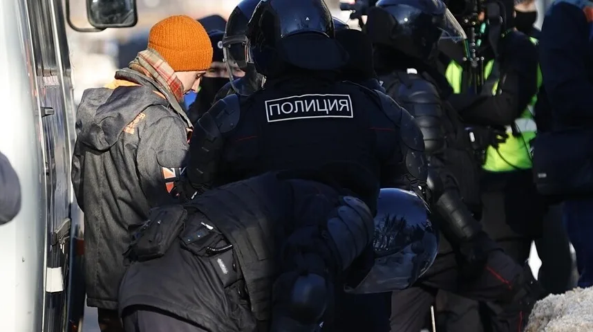 Policajci u punoj opremi, na čijim uniformama piše 'ПОЛИЦИЯ', hapse muškarca obučenog u narandžastu kapu i jaknu.