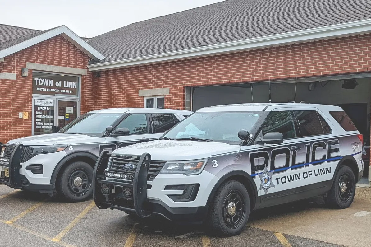 Dva bijela policijska vozila sa natpisom "POLICE TOWN OF LINN" ispred zgrade opštine Linn.