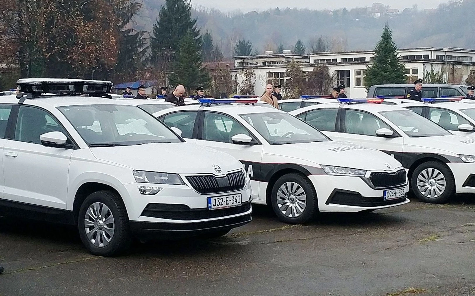 Bijela policijska vozila marke Škoda sa upaljenim rotacionim svjetlima parkirana u nizu.
