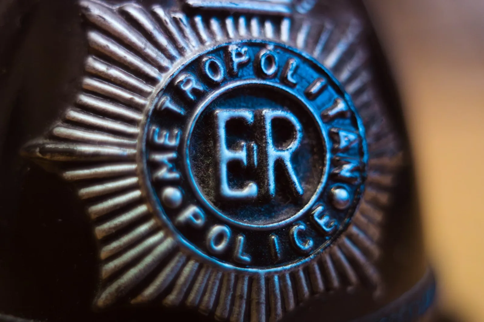 Krupni kadar metalne policijske značke sa natpisom "METROPOLITAN POLICE" i inicijalima "ER" u sredini.