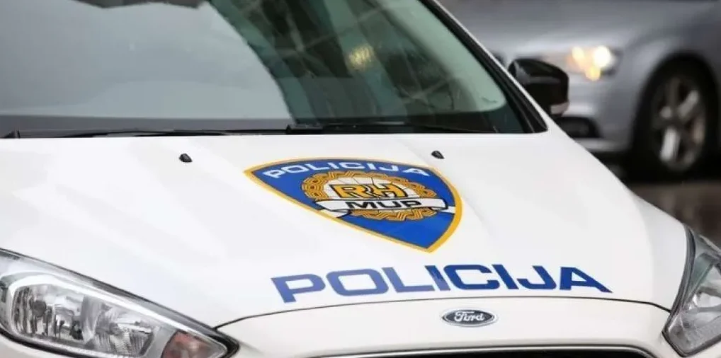 Bijelo policijsko vozilo marke Ford sa oznakom policije i grbom na haubi.